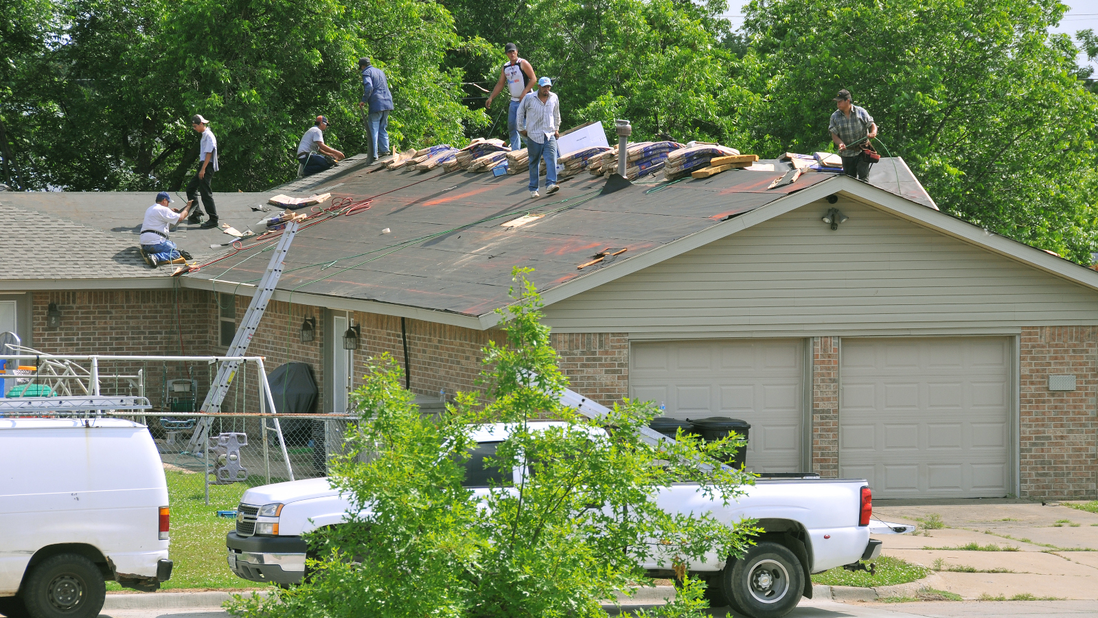 A roofing crew replaces a roof's shingles on a home with damages from a tornado.