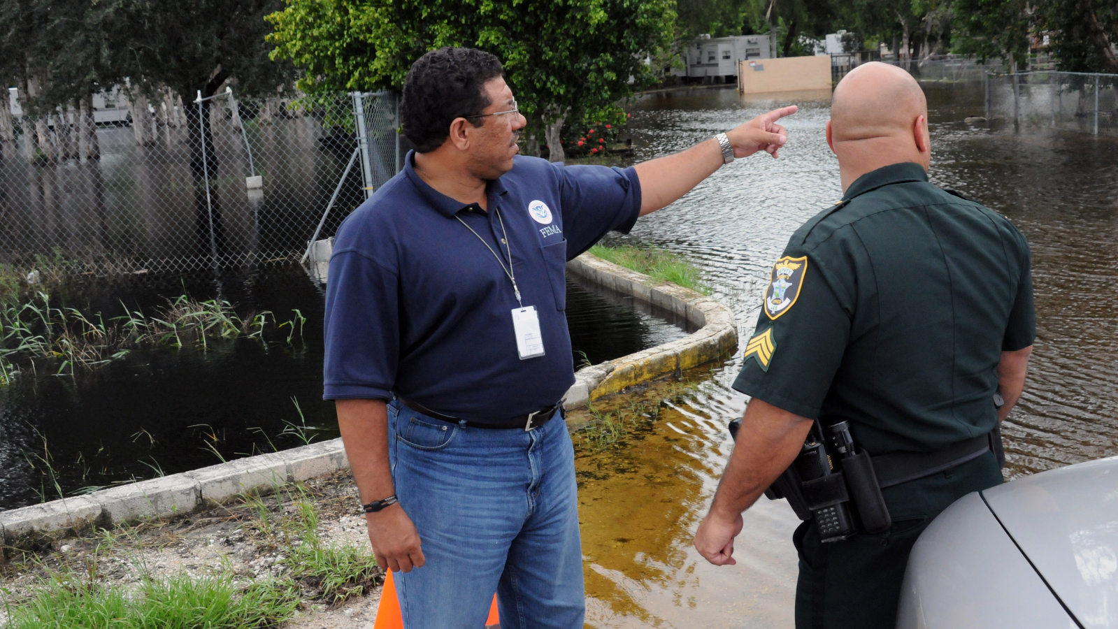 High catastrophe losses led to FedNat%27s rate hike, which occur in the wake of hurricanes like flooding from Tropical Storm Fay that brought FEMA Public Information Officer William Lindsey and Lee County Sheriffs Officer to a flooded development. - By George Armstrong/FEMA Photo Library